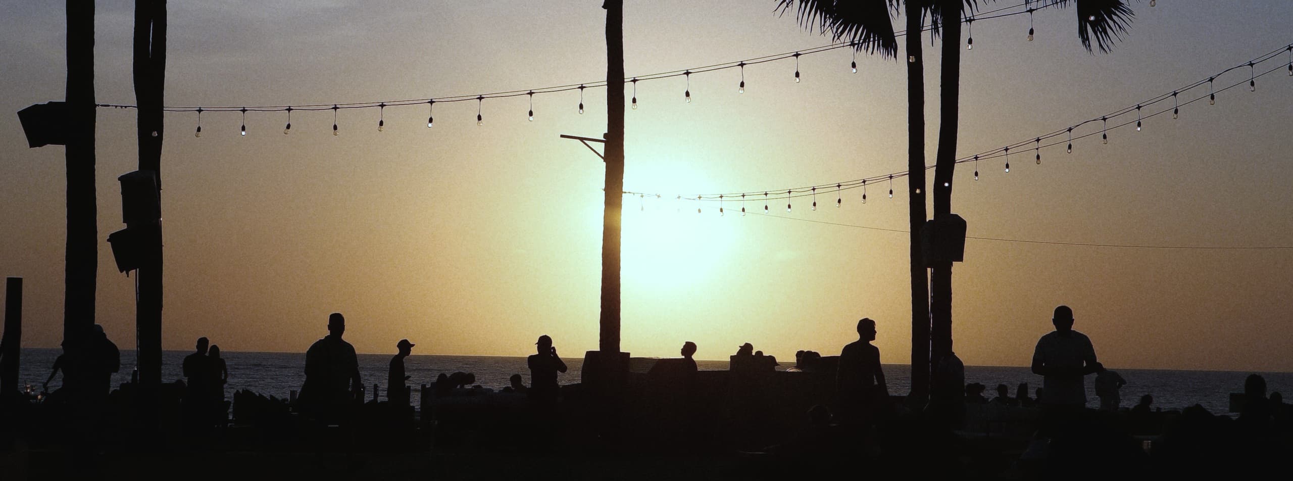 Palmen und Gäste als Silhouetten im Sonnenuntergang am Meer