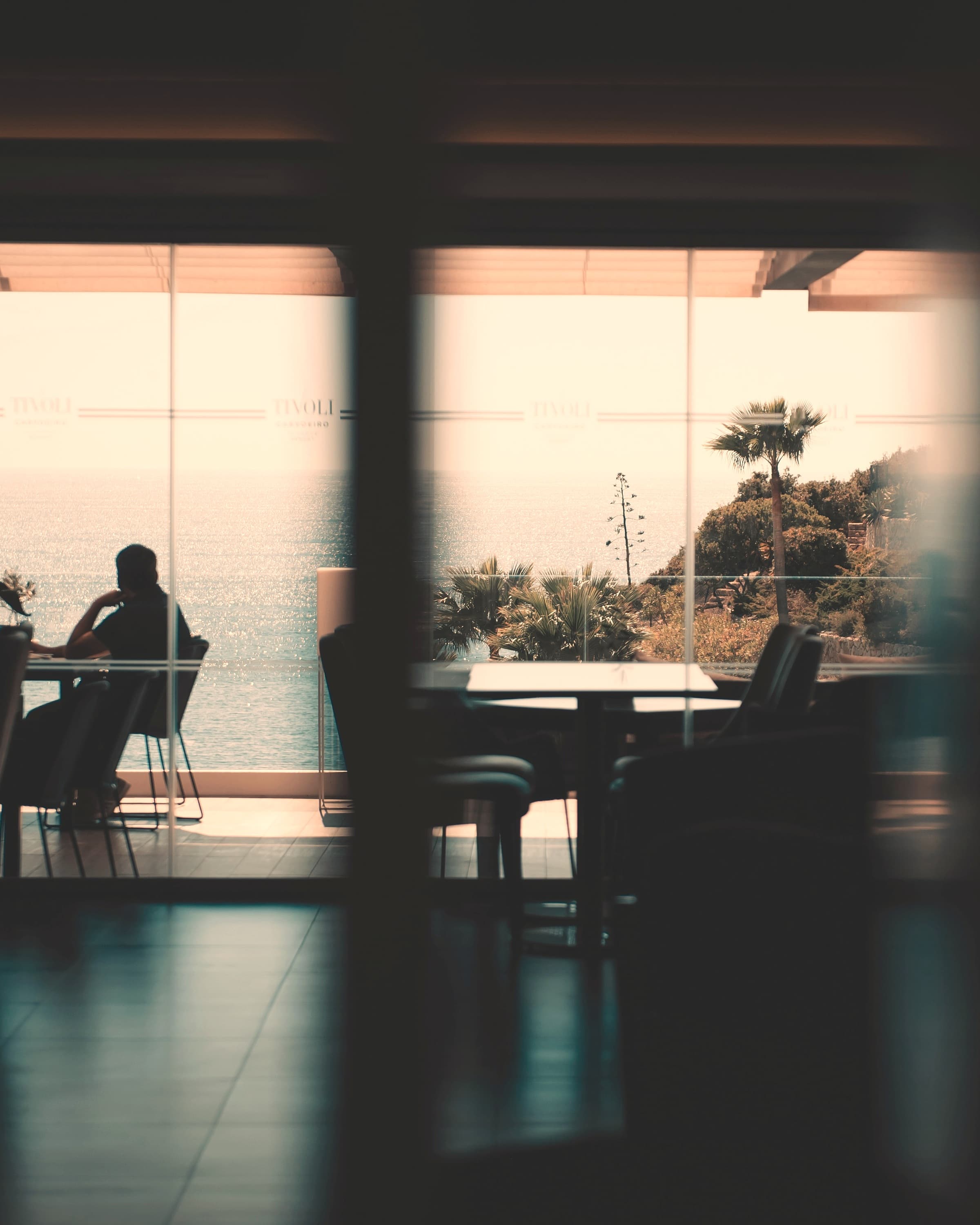 Blick durch eine Glasfront auf das Meer, Gäste an den Tischen
